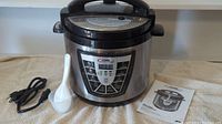 Power Brand Pressure Cooker XL with power cord, rice paddle, and manual on a white towel.