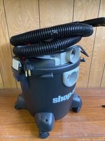 Front and angled view of Shop-Vac wet/dry vacuum with hose wrapped on top, showing brand logo and cord plug.