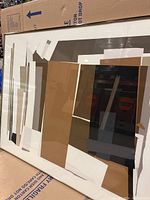 Framed abstract art print with geometric shapes in brown, black, white, and beige tones, leaning against a cardboard box.