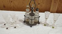 Wide view of the entire lot including silver plated condiment server with four cut glass bottles and stoppers, 4 Stuart Crystal dessert wine glasses, and 2 Cavan Full Lead Crystal sherry glasses arranged on white cloth.