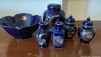 Group photo of six cobalt blue Japanese porcelain items on wooden surface, showing bowl, ginger jar, two small urns, and two small flower vases with floral patterns.