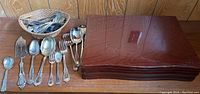 Photo showing the Nobility Plate flatware set arranged alongside a basket of mixed silver plate flatware and a polished wooden flatware box.