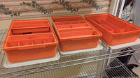 Three vintage orange Tupperware organizer containers placed side by side on a wire rack shelf, showing total set of three items with various removable orange trays inside.
