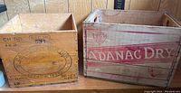 Side by side view of two wooden crates, Canadian Butter on the left and Adanac Dry on the right, on a wooden shelf