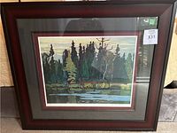 Framed art print showing a forest and water, dark wood frame with decorative edge