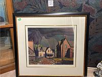 Full view of the framed artwork showing a village scene with houses under a thunderstorm sky.
