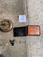 Image showing the entire lot including a vintage brass ashtray, two handmade leather wallets (black and brown), a Philippine scarf holder with a bull-head design, and a vintage key.