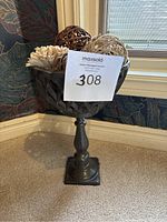 Front angle showing entire cast iron garden pedestal urn planter with decorative balls inside bowl, note lattice design and scalloped rim.