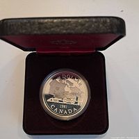 Photo of the 1981 Canadian silver dollar coin displayed upright in a burgundy velvet-lined black presentation box showing the train design on the coin.