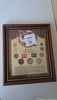 Frontal view of the entire framed British World War II coin collection showing the layout of coins, two stamps, and decorative flag and aircraft illustration.