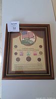 Full view of framed United States World War II collection showing coins and stamps mounted on decorative paper background with American flag and tank illustration.