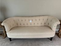Front view of an off white tufted couch with rounded armrests and dark wooden legs.
