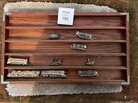 Metal miniature train cars and engines displayed in wooden cabinet with horizontal slots.