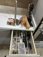 Open kitchen drawer containing assorted flatware (forks, spoons), graters, a peeler, and various utensil handles and blades.