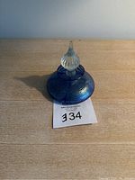 Image of an iridescent blue and purple pulled feather glass perfume bottle with a tall, clear stopper shown on wooden surface.