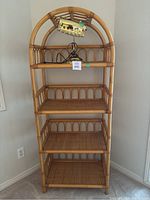 Front view of rattan shelving unit with four shelves and desk lamp on top shelf