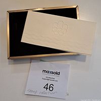 Box with black velvet lining and a cream-colored embossed Olympic rings sleeve placed on top.