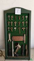 Overall view of the mounted display board with keys, plaque, wrench, pipe fitting, and metal brackets on green background.