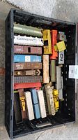 All model train cars and accessories packed inside a black plastic crate placed on the ground.