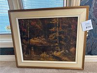 Framed vintage oil painting of forest landscape resting on floor near window and floral wallpaper.