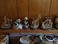 Shelf overview showing six Andrea by SandeK porcelain animal figurines: rabbits, two pandas, deer stag, deer family, wolf-like creature