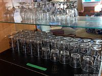 Photo showing two shelves of various cocktail and stemware glasses, clear glass with gold and black decorative trim.