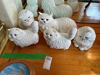 Front view showing all five white ceramic cat figurines grouped together on the floor, highlighting their similar size and design.