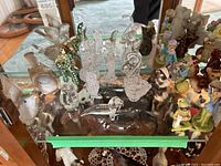 Glass animal and bird figurines on glass shelf including clear, textured, and multi-colored items along with some ceramic and china figurines visible.