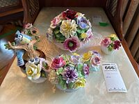 Six porcelain decorative figurines including five floral arrangements and one Blue Jay bird figurine on a table with lace doily.
