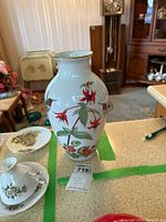 Front view of porcelain vase decorated with red flowers and green leaves, showing hummingbirds on the body.