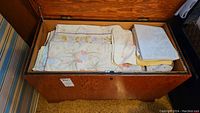 Overview of a wooden chest filled with folded linens including towels and bedding showing various patterns and colors.
