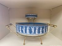 Front view of large and small glass serving bowls on gold-tone metal holder stands, showcasing blue band with white classical figure motifs.