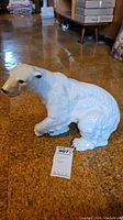 Full side view of the white ceramic polar bear figurine sitting on a wood floor showing the entire figure and part of the textured fur details.