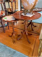 Two wooden side tables with scalloped edges and pedestal legs on a wooden floor.