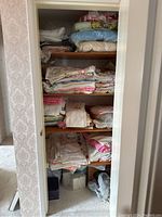 Shelf of various folded table linens, towels, blankets and doilies arranged inside a closet.