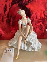 Front view of porcelain figurine showing seated lady wearing ruffled dress tying shoe