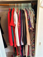 Photo of assorted vintage blouses, dresses, suits, and sweaters hanging neatly on hangers in a closet rod, showing diverse colors and patterns.