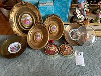 Eight pieces of framed wall art, including china plates with classical couple scenes and pressed flower artwork, all with gold-toned framing.