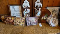 Full view of lot items including two tall sculptured plaques, multiple smaller animal-themed plaques, framed cross stitch poem, and wooden plaque.