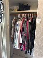 Closet view showing mixed blouses and blazers on hangers, various patterns including floral, plaid, polka dots, and solid colors.