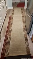 Full length view of the 119 inch runner rug laid in a narrow hallway or kitchen space, showing beige center with floral patterned sides and red outer border
