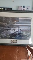Full view of the framed print showing a lakeside scene with water lilies and ducks, with trees in background and plaque on bottom frame.