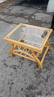 Bamboo side table with clear glass top on outdoor pavement, showing front and side curved bamboo design