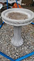 Front and top view of the stone bird bath placed on gravel with visible basin surface and raised edge.