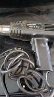 Black and Decker Heat 'N Strip electric heat gun showing label and power cord, placed on a black surface.