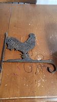 Cast iron rooster wall hanger on wooden surface showing detailed rooster figure and curled hanging arm.