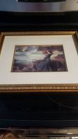 Full view of the framed "Miranda" picture showing the subject standing on cliff near ocean with waves and cloudy sky, in gold-tone decorative frame.