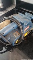 Side angle of blue Ryobi belt sander with cord wrapped around and visible label.