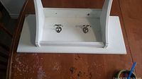 Top view of white wooden wall shelf with two silver hooks on underside.