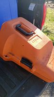Photo showing the orange Stihl carrying case with black handle and logo on lid, placed in truck bed.